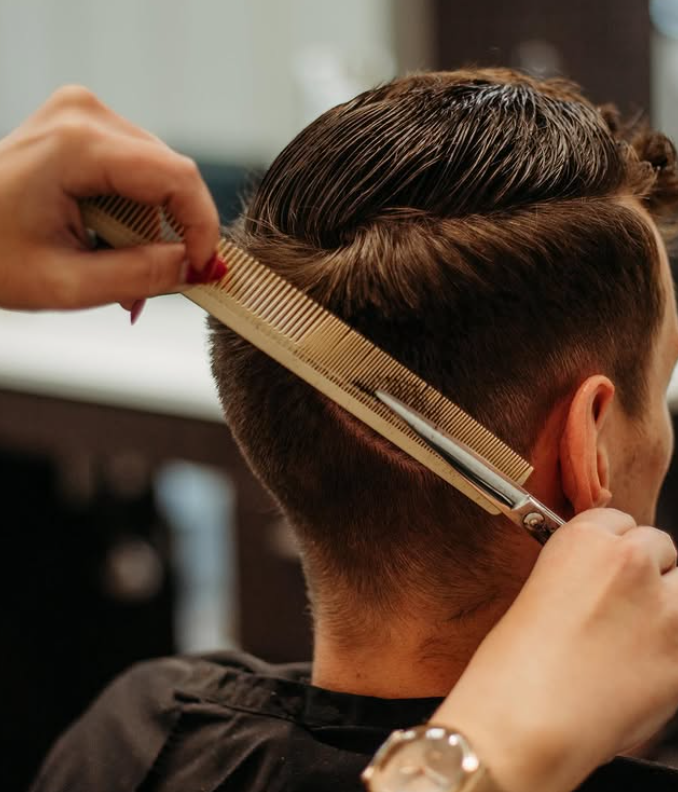 A person receives a haircut as a stylist uses a comb and scissors to trim the hair near the ear. -Pure Salon, Ankeny, Johnston, & Indianola, IA