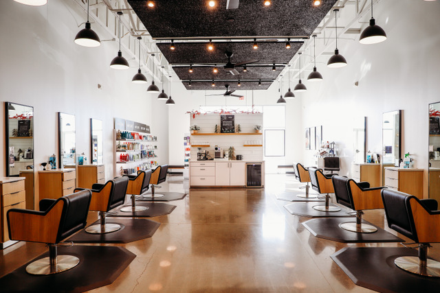 Modern hair salon interior with empty styling chairs, large mirrors, shelves stocked with hair products, and bright overhead lighting. -Pure Salon, Ankeny, Johnston, & Indianola, IA
