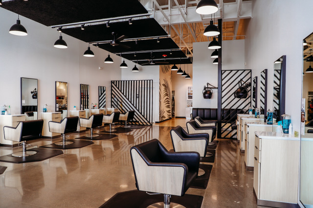 Modern hair salon interior with empty black and beige styling chairs, mirrors, hair dryers, and minimalist decor featuring black geometric wall patterns. -Pure Salon, Ankeny, Johnston, & Indianola, IA